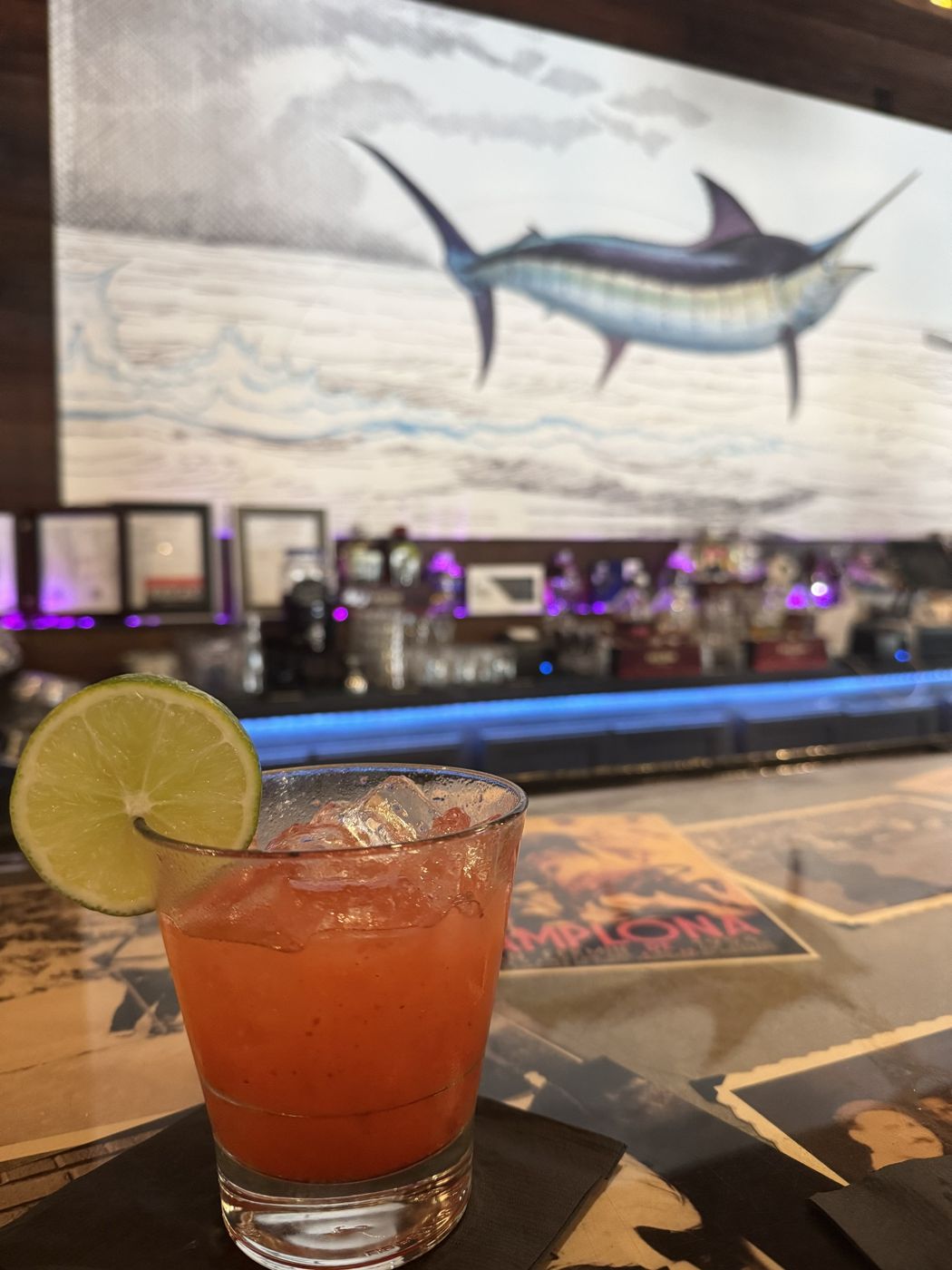 Red cocktail with a lime wedge at a bar with a marlin mural